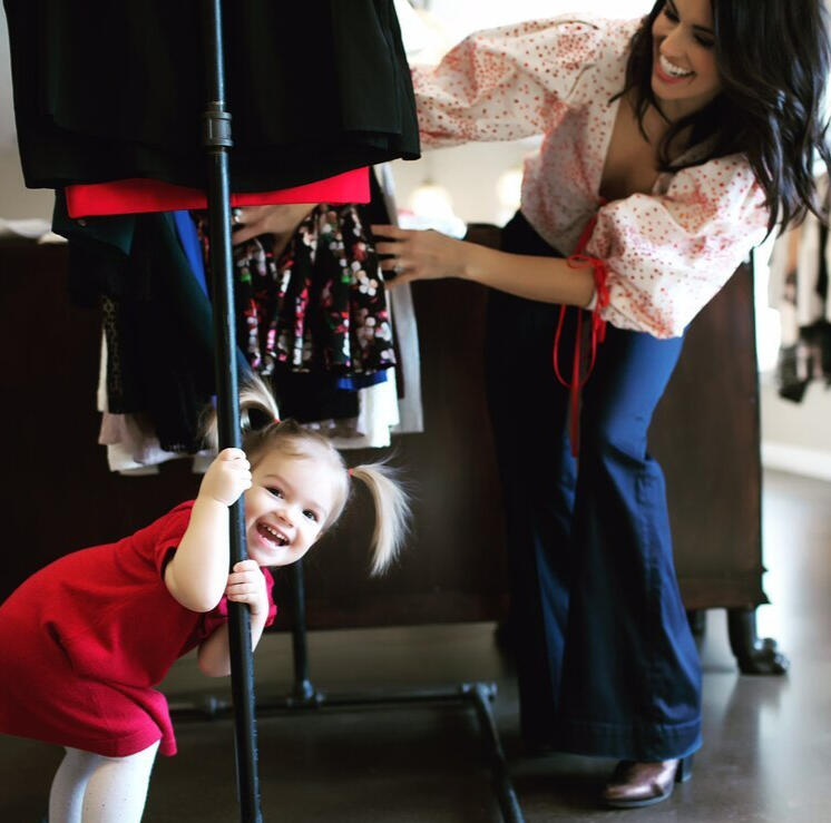 Lena Piskorowski looks at a clothing rack while her young daughter hides within the clothes.