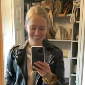 blonde young woman is smiling taking a selfie of her wearing a black moto jacket